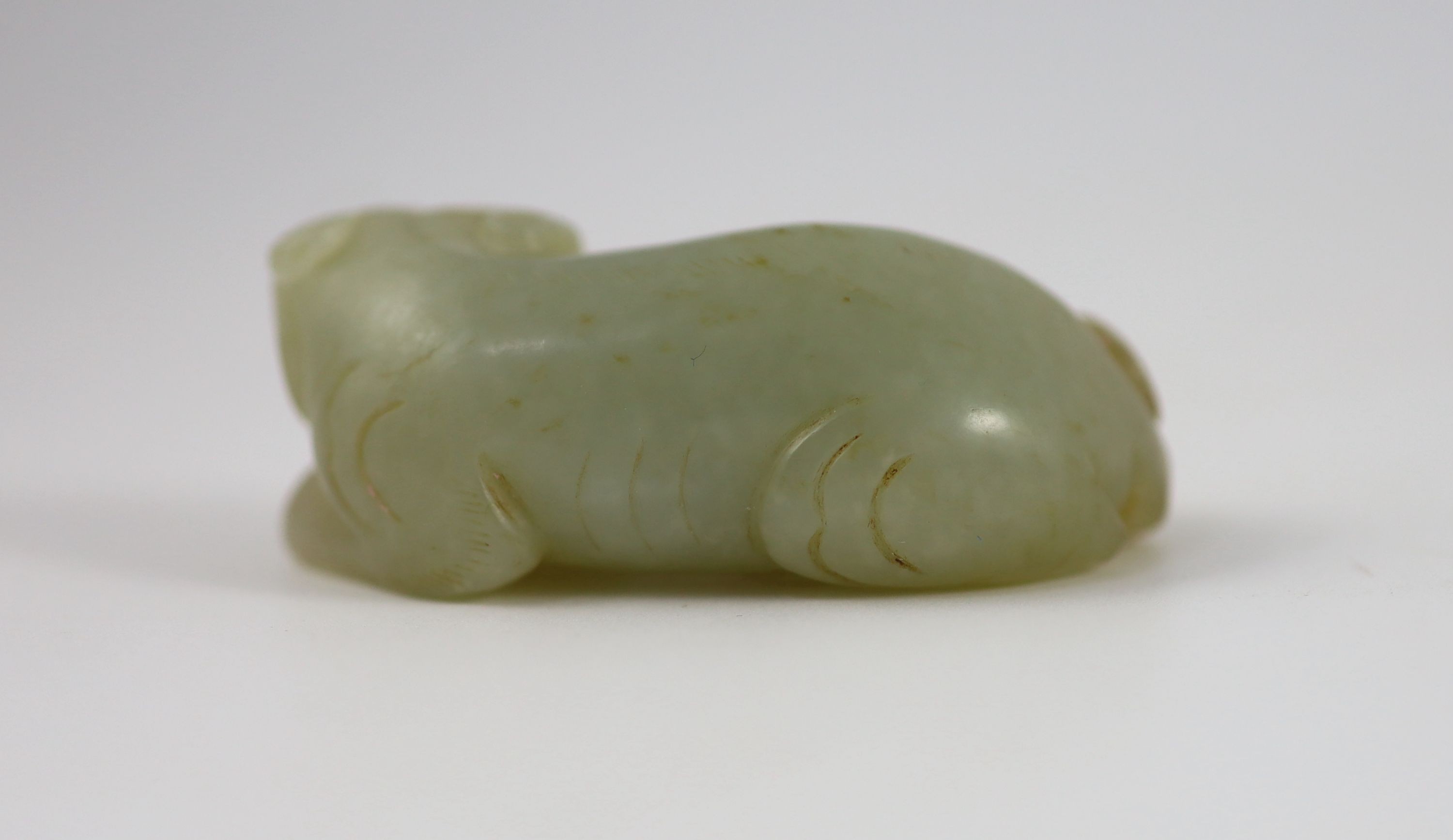 A Chinese pale celadon and russet jade figure of a lion dog, 6.2 cm long